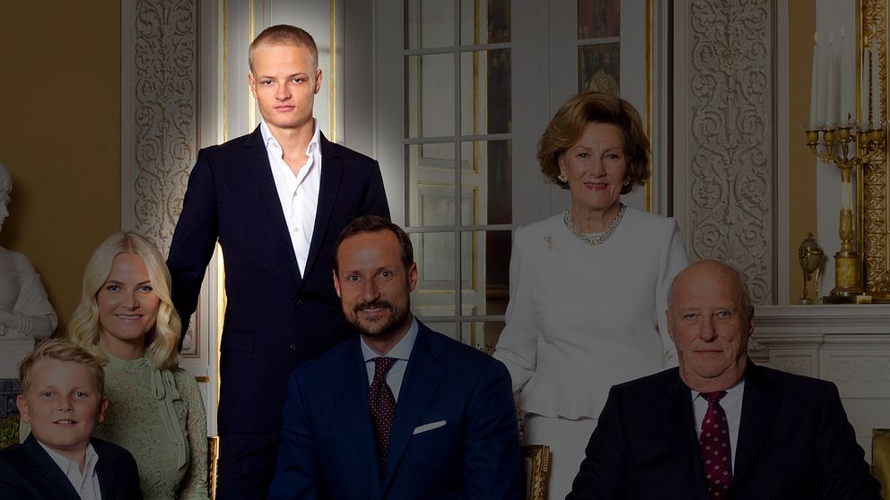Gruppfoto av norska kungafamiljen klädda i formella kläder, samlade i en elegant inomhusmiljö med ljusa väggar och stiliga inredningsdetaljer. En person (Marius Borg Høiby) står i mitten.
