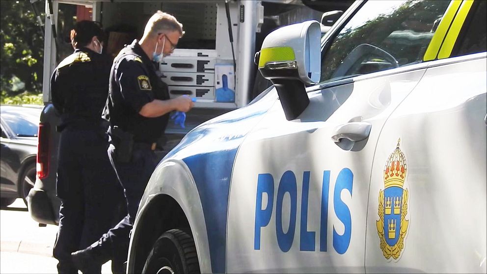 En polisbil står parkerad. En polis går i bakgrunden.
