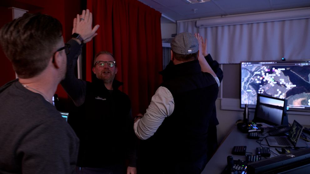 Flera personer ger varandra high five framför datorer i ett övervakningsrum.