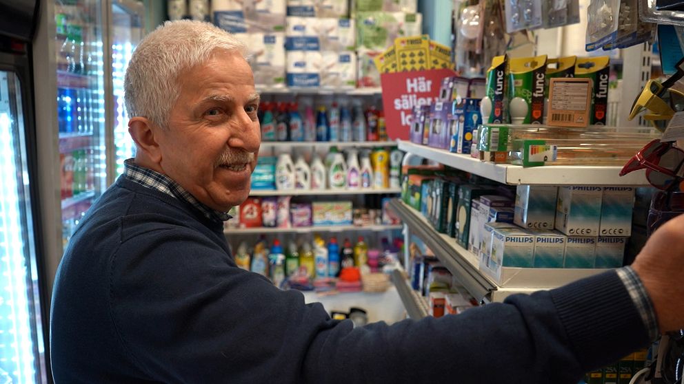 Man står framför butikshyllor med hushållsprodukter och livsmedel.