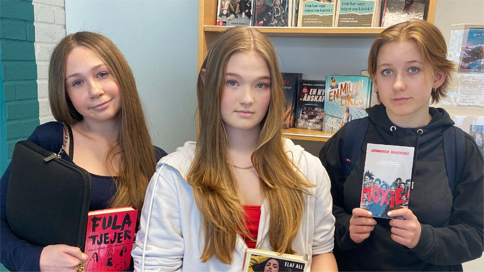 Emma Slagbrand, Anabelle Touminen och Amanda Dahl står framför en bokhylla och håller varsin ungdomsbok. De tycker att det är synd att allt färre ungdomsböcker ges ut.