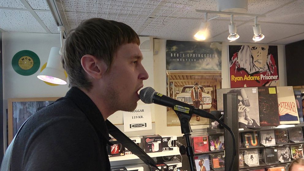 Tomas Stenström sjunger vid mikrofon i en skivbutik.