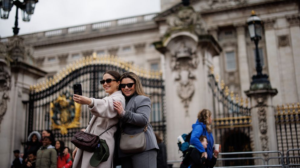 Två kvinnor tar en selfie framför Buckingham Palace.