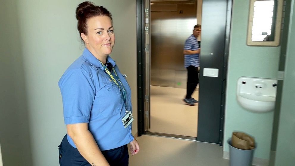 Kvinna i blå uniform inne i en häktescell med ljusgröna väggar