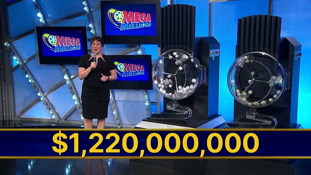 En programvärd står framför två lotterikuponger och en stor skärm med texten ”Mega Millions”. En stor summa, $1,220,000,000, visas tydligt i bildens nedre del, vilket indikerar det aktuella jackpotbeloppet.