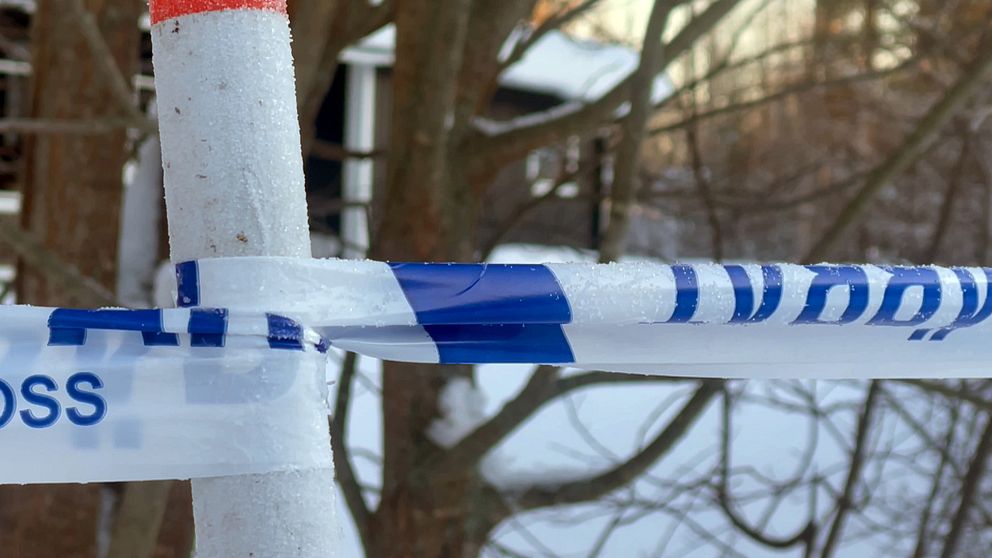 Polisavspärrning med rimfrost omger ett område bland vinterträden. I bakgrunden syns ett hus.