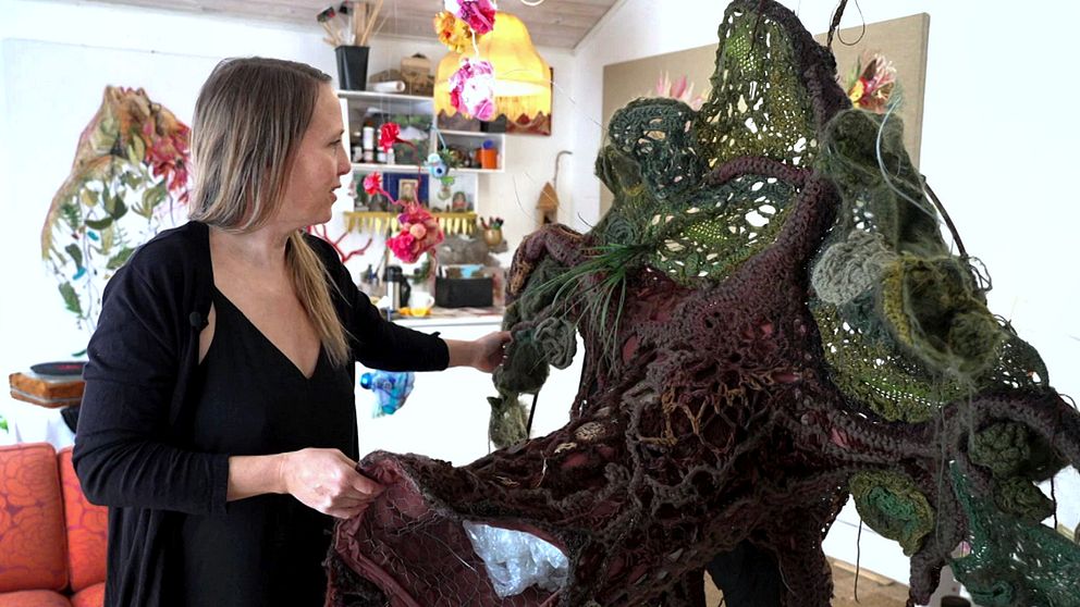 Kvinna visar detaljer från sin konstskulptur i ett färgglatt rum.