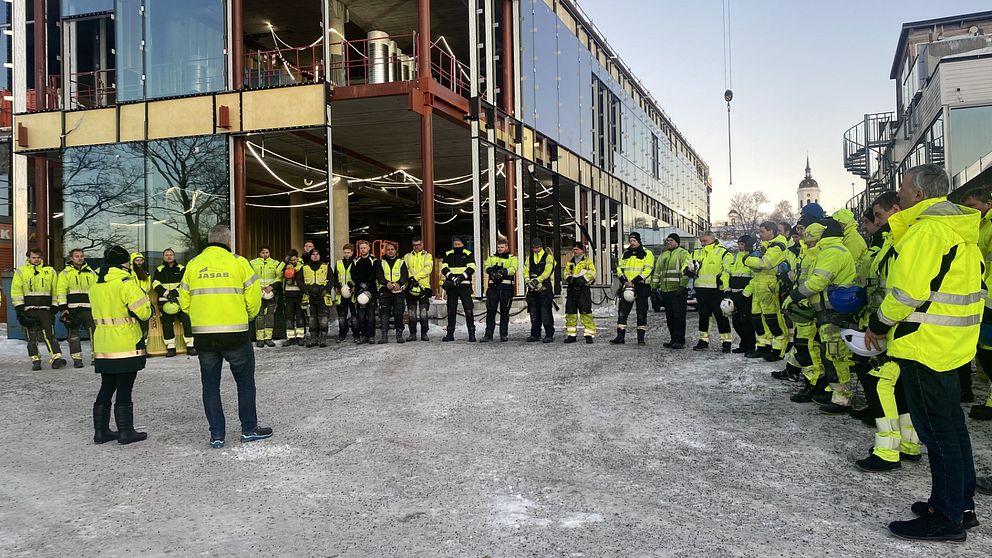 På bilden syns flera personer som är iklädda varselkläder på ett bygge i Härnösand. De har tagit av sina hjälmar och håller en tyst minut efter hissolyckan i Sundbyberg förra veckan.