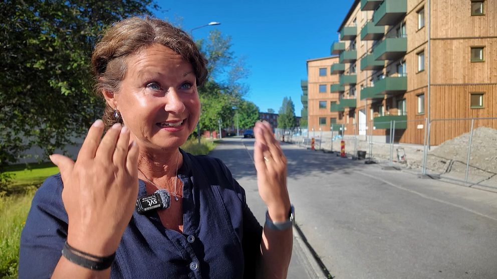 Person gestikulerar på gata med nybyggda bostadshus i bakgrunden en solig dag.