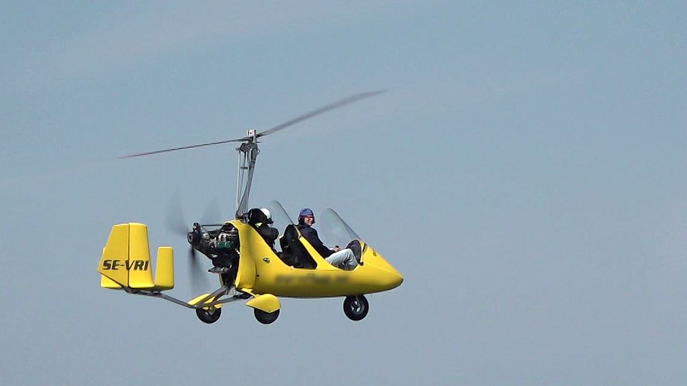 En gul gyrokopter, med öppen kabin, flyger.