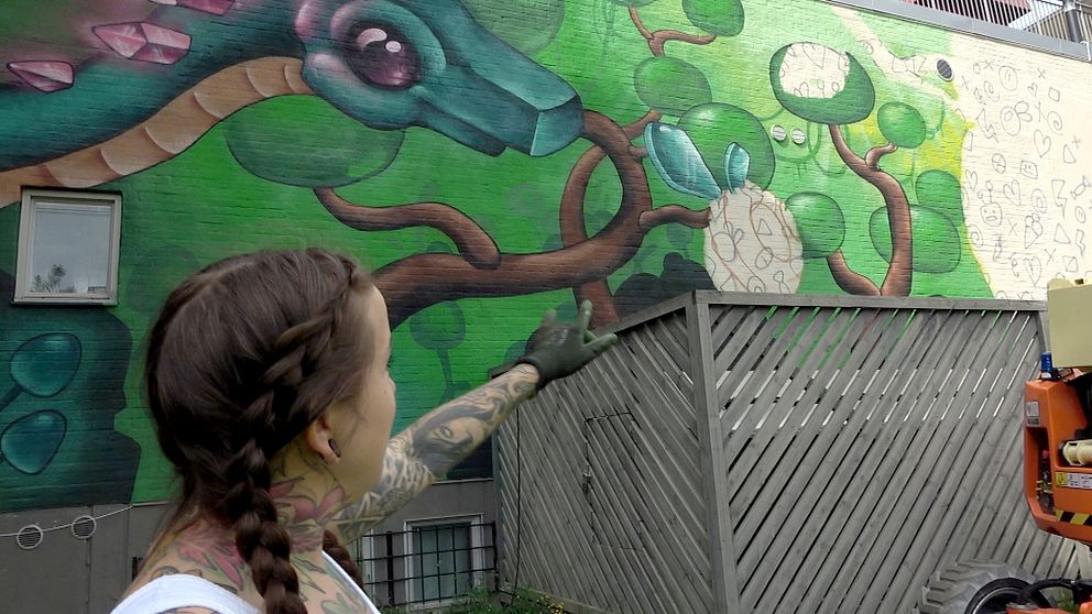 Konstnären Victoria Sundqvist pekar på en halvfärdig muralmålning med ett tillhörande ”doodle grid”.