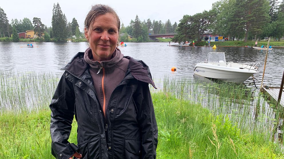 Funktionären Stina Munters står vid älvkanten i Vansbro.  I bakgrunden simmar folk.