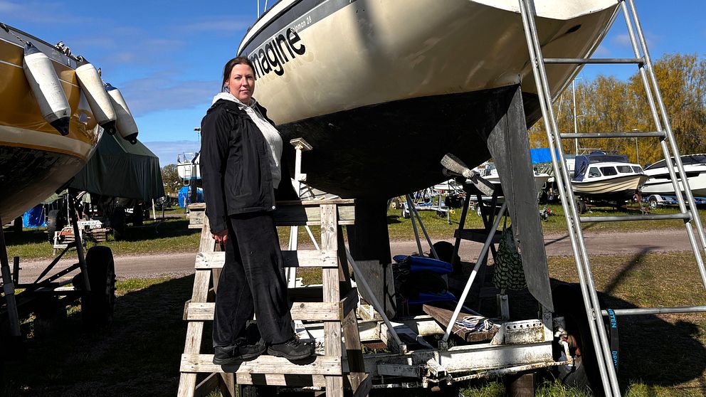 En person står på stege vid en uppställd segelbåt på en uppläggningsplats.