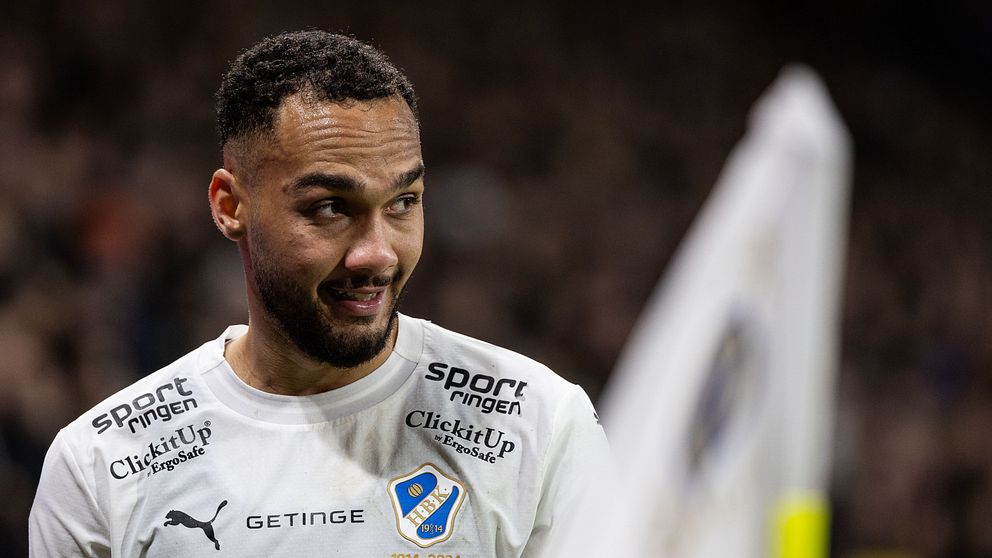 Fotbollsspelare i vit tröja på plan med en hörnflagga i bakgrunden.