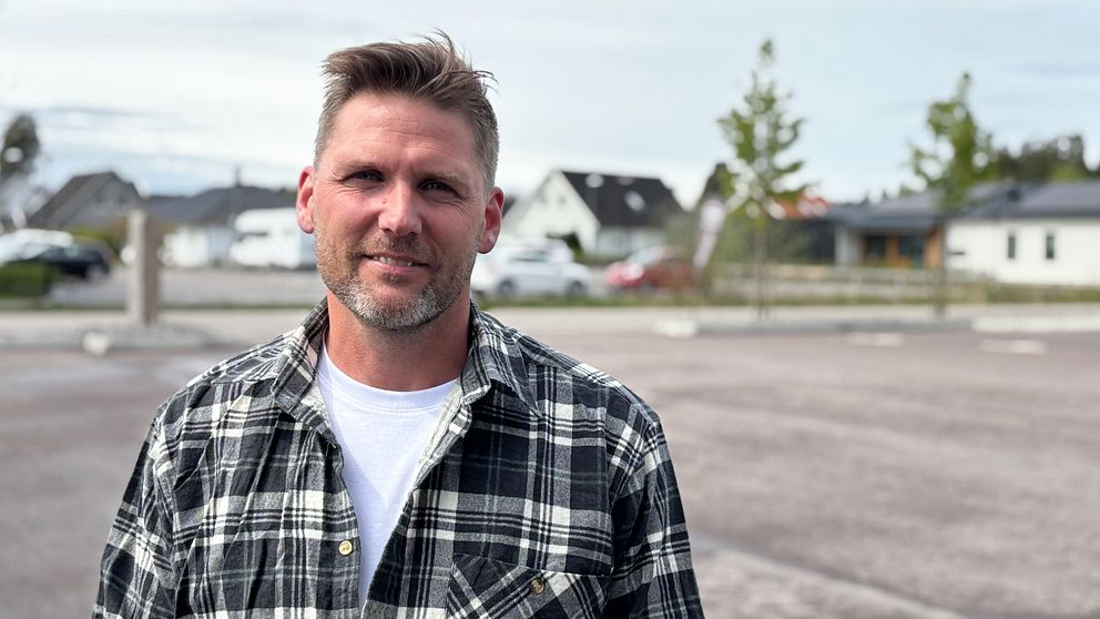 Person i rutig skjorta står på en tom parkering med hus i bakgrunden.