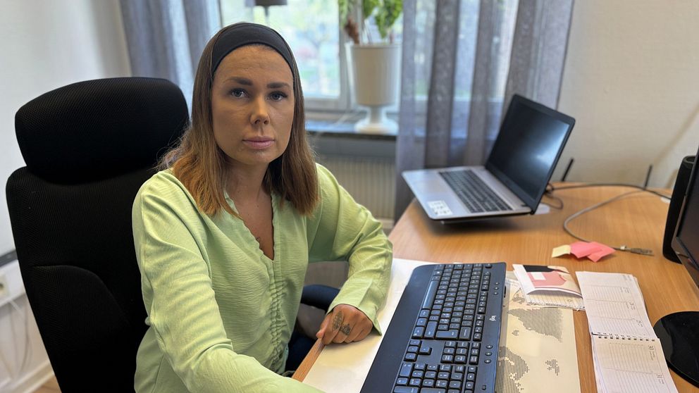 Kvinna i ljusgrön skjorta sitter vid ett skrivbord med dator och anteckningar.