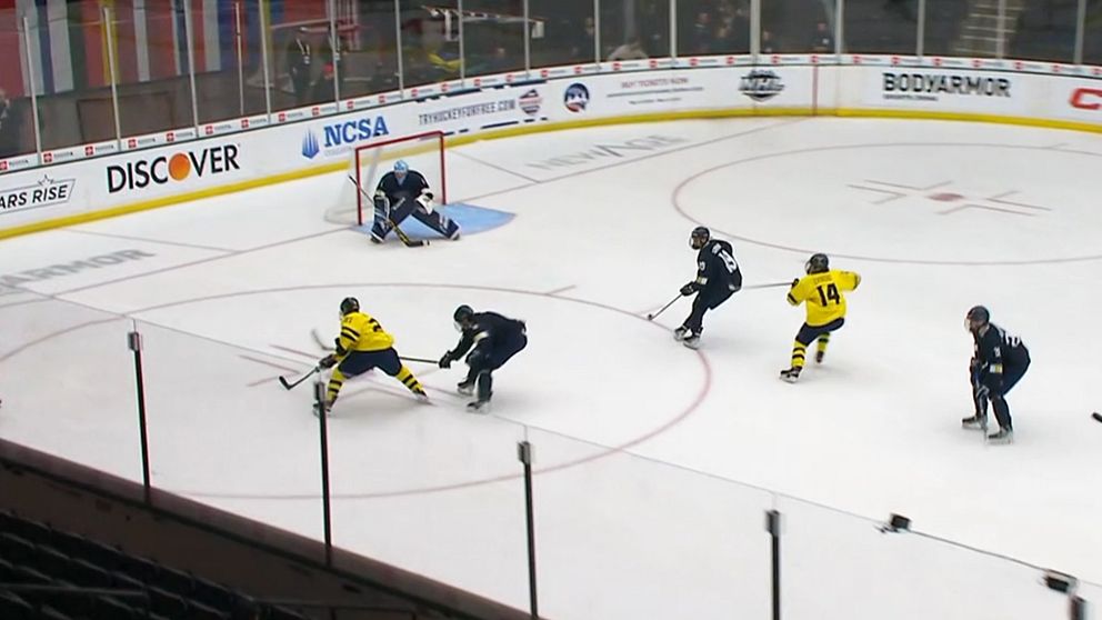 Ishockeyspelare i gul tröja skjuter mot mål, försvarare och målvakt försöker stoppa pucken.