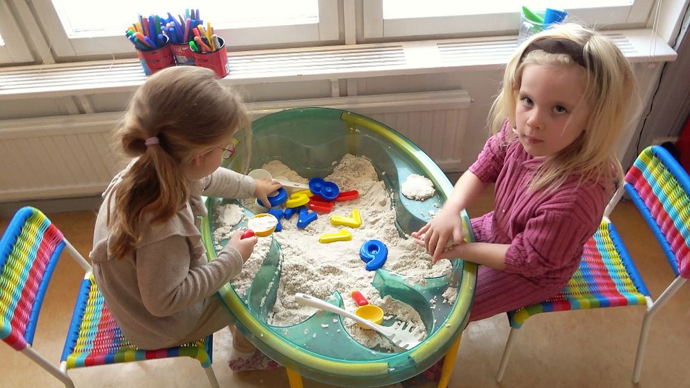 Två förskolebarn på Bollsta förskola som leker med sand. I sanden ser man olika former och siffror i plast,