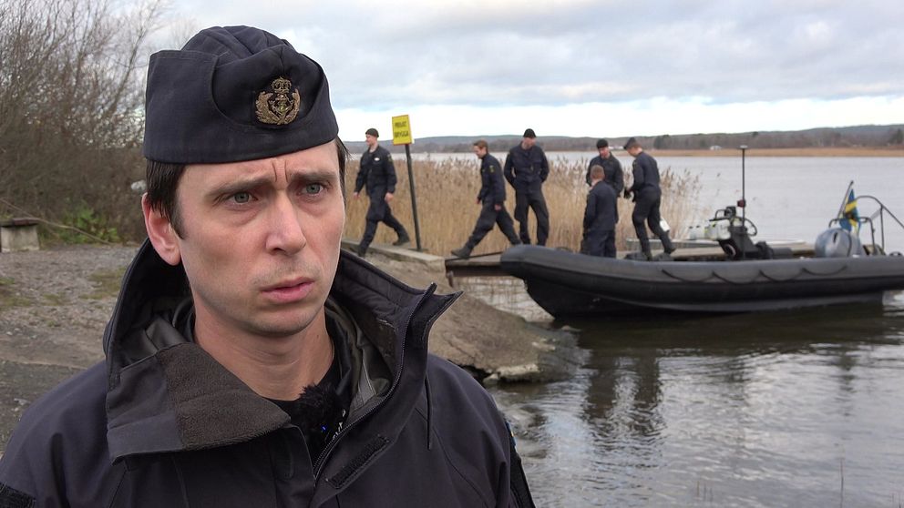Kapten Karl Ekman framför röjdykare och en gummibåt i strandkanten