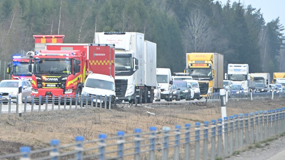 Trafikkö med lastbilar och personbilar på E20, skog i bakgrunden.