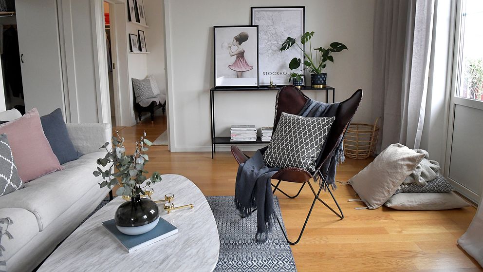 Modernt inredd vardagsrum med soffa, fåtölj och dekorationer på bord och hylla.