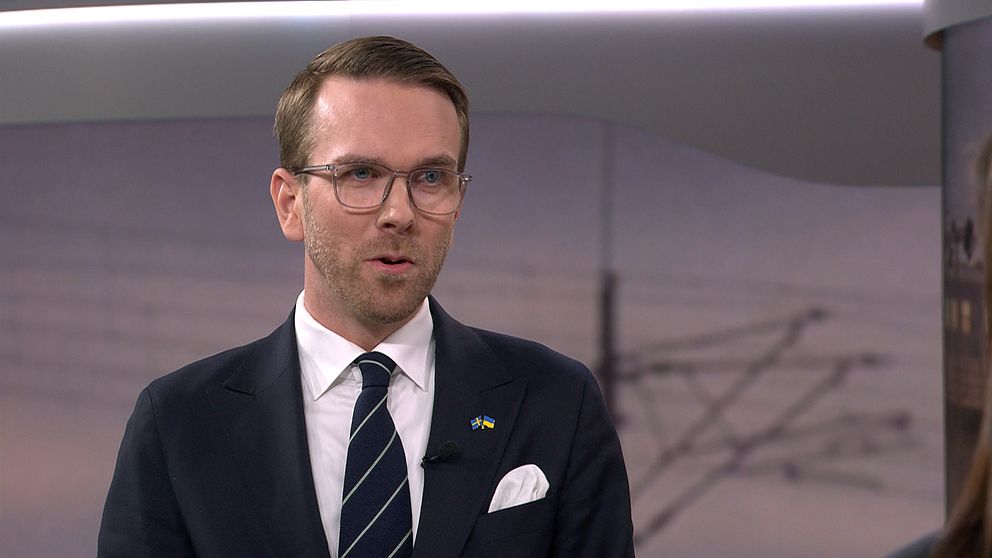 Man i kostym och glasögon står i en tv-studio.