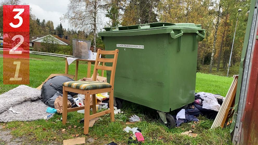 Gamla möbler och tyger ligger slängda framför en grön container.