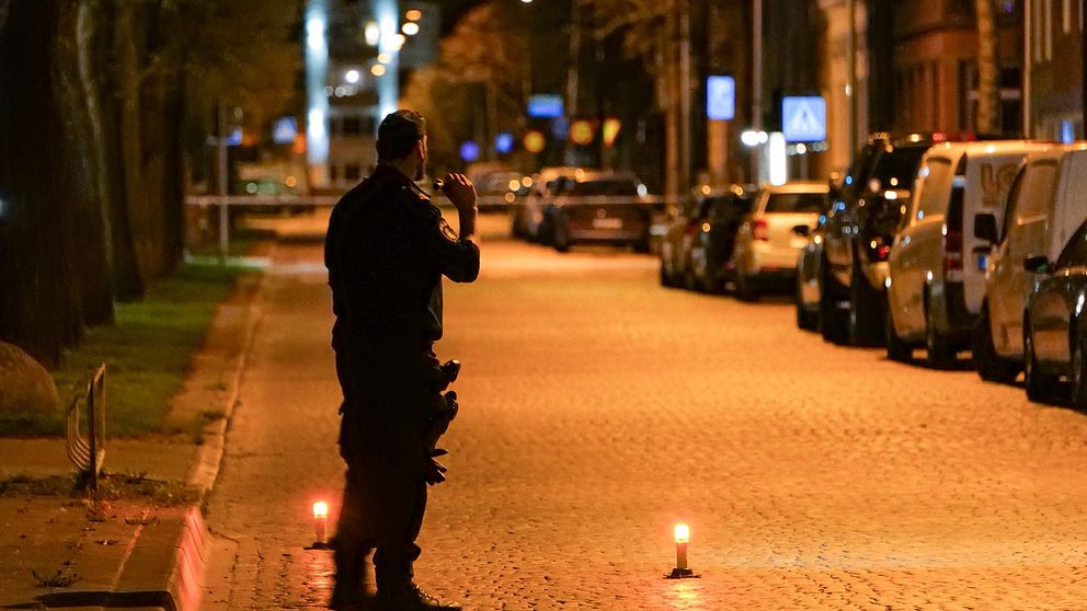 polis står på en avspärrad gata och lyser med en ficklampa