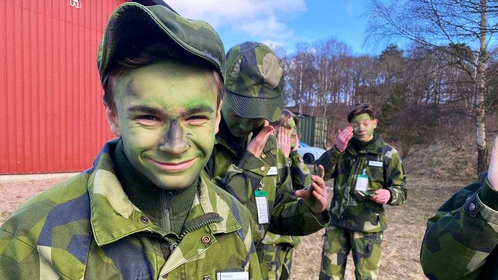 Praoelever i kamouflageuniformer utanför en röd byggnad.