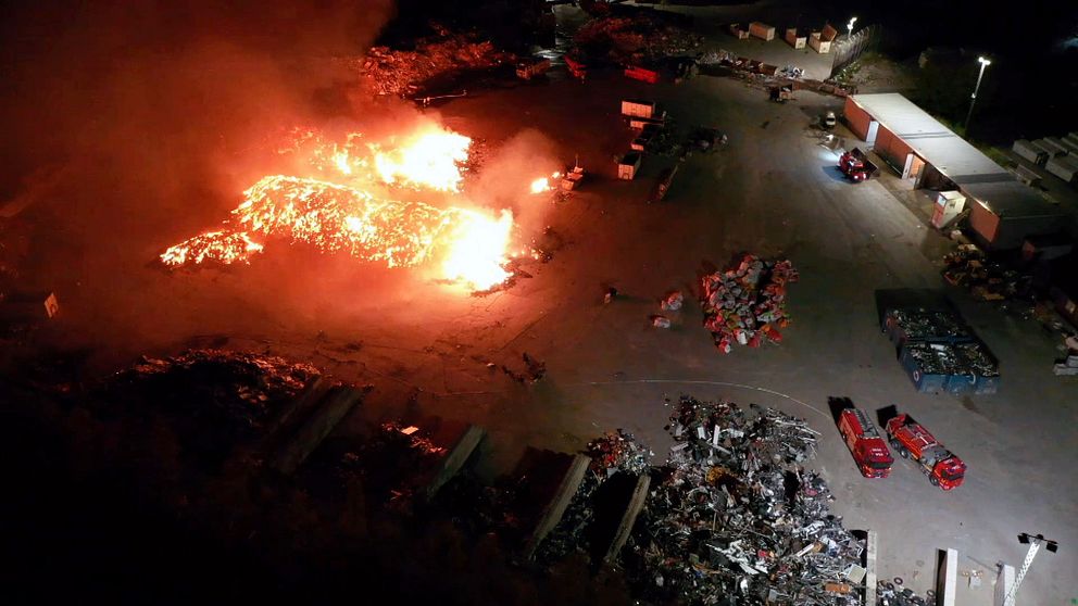 Stora lågor vid en brand på en återvinningscentral nattetid. Räddningstjänst på plats.