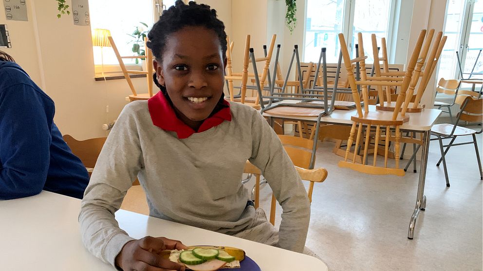 En pojke sitter vid ett bord och håller i en smörgås.