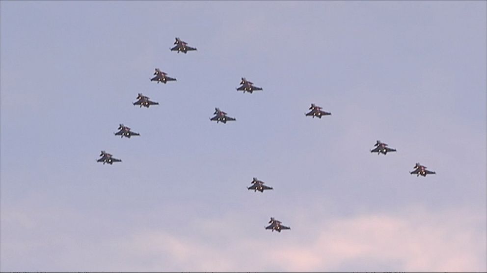 Flera stridsflygplan flyger i formation på en klar himmel, arrangerade i en synlig V-form.