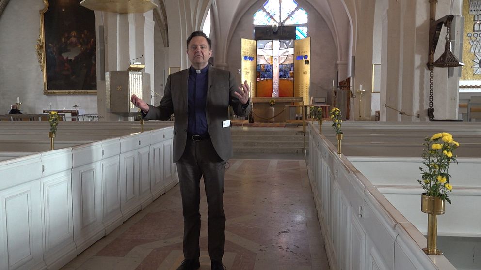 En präst står i en kyrka och håller ut sina armar