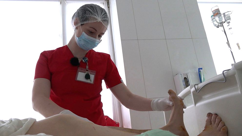 En kvinna iklädd sjukhuskläder böjer försiktigt på en patients fot