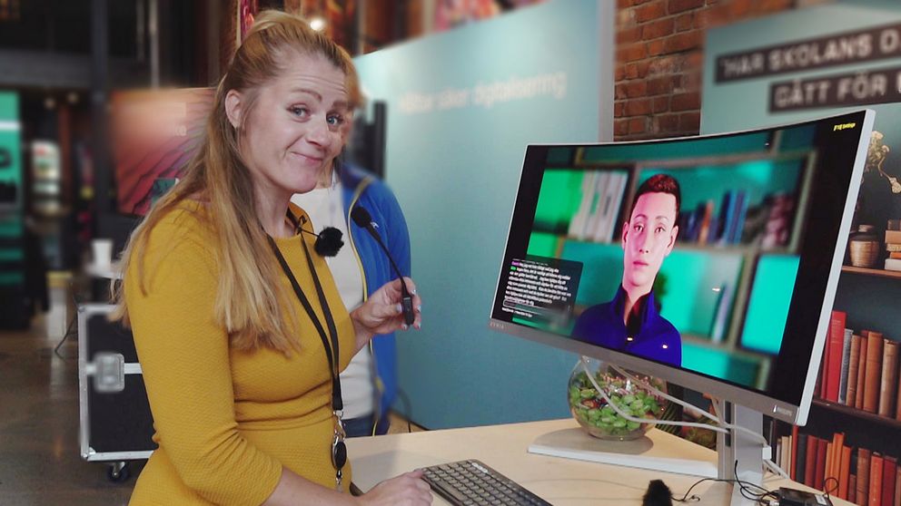 Reportern Otilia Bogen tittar in i kameran. Hon håller i en liten mikrofon som är kopplad till en datorskärm där ett AI-ansikte syns.