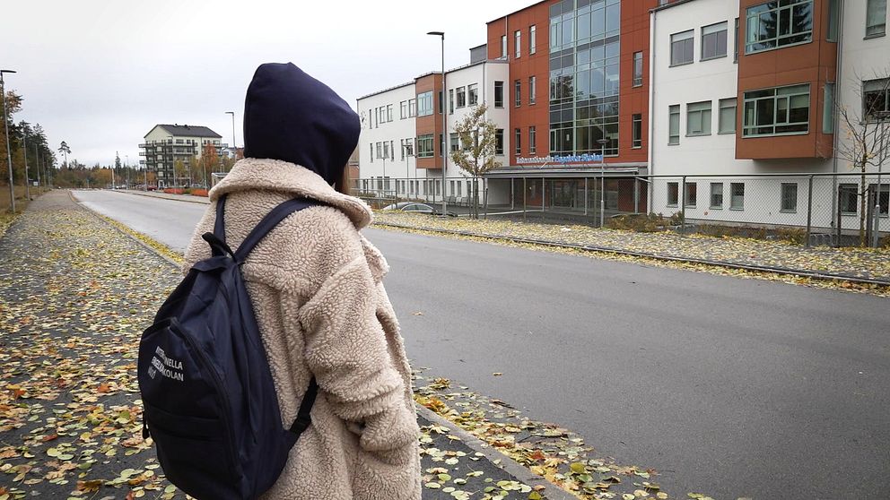 En elev med ryggsäck och huvan uppe står utanför Internationella engelska skolan i Växjö