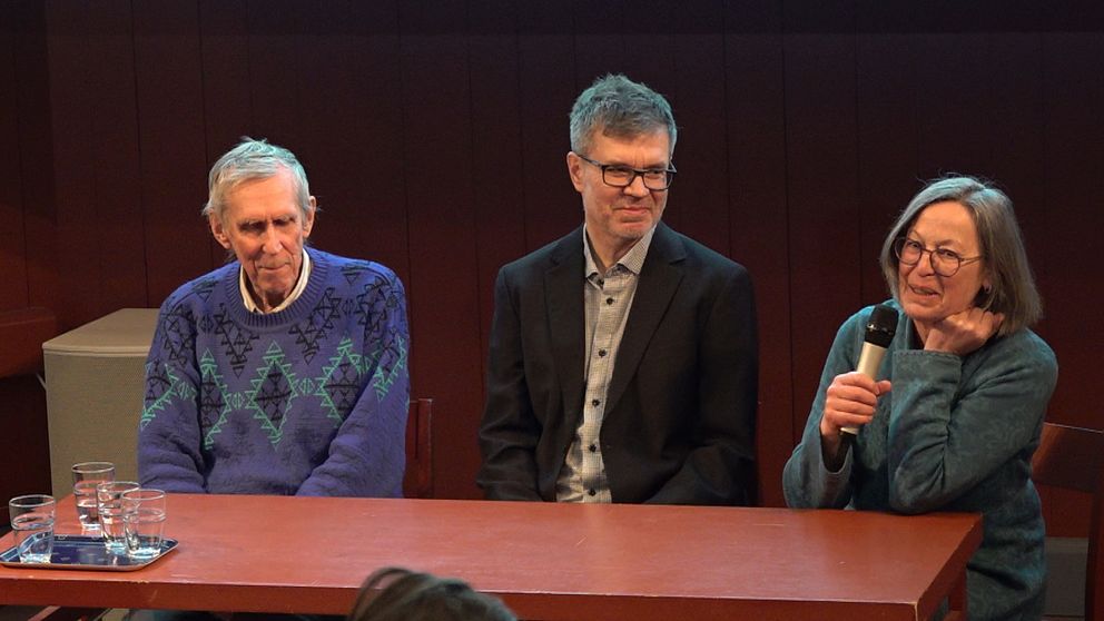 Tre personer sitter vid ett bord, en håller i en mikrofon.