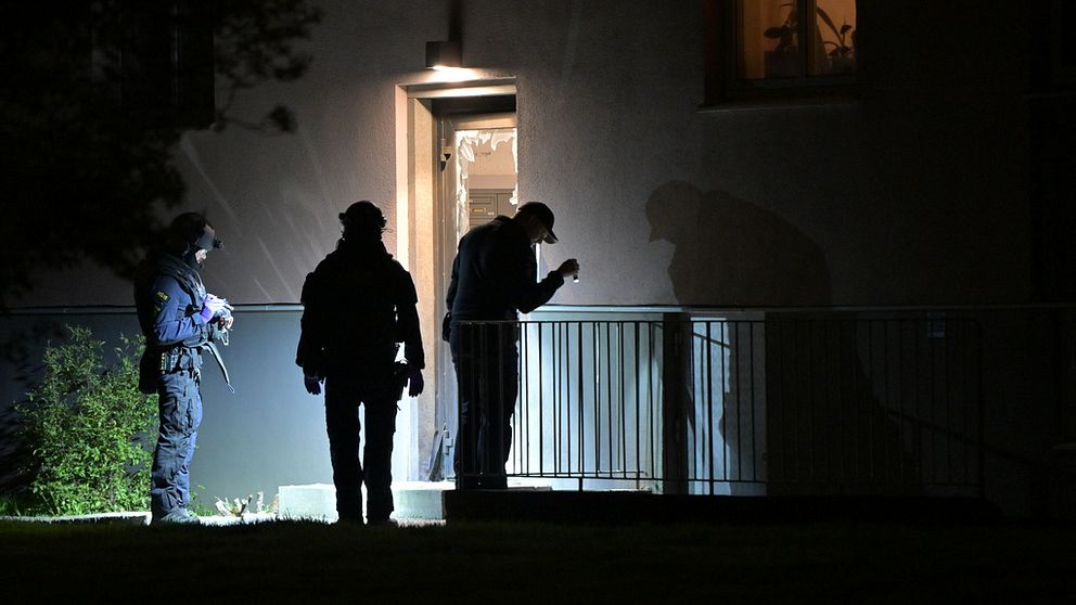 Poliser undersöker en bostadsingång i mörker med ficklampor.