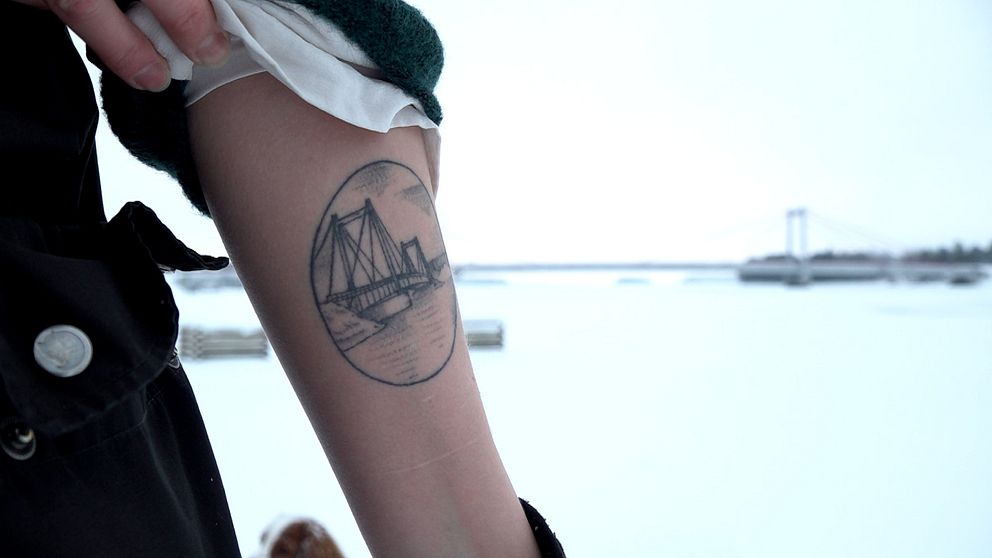 En taturerad underarm med Strömsundsbron som motiv. I bakgrunden syns den fysiska bron.