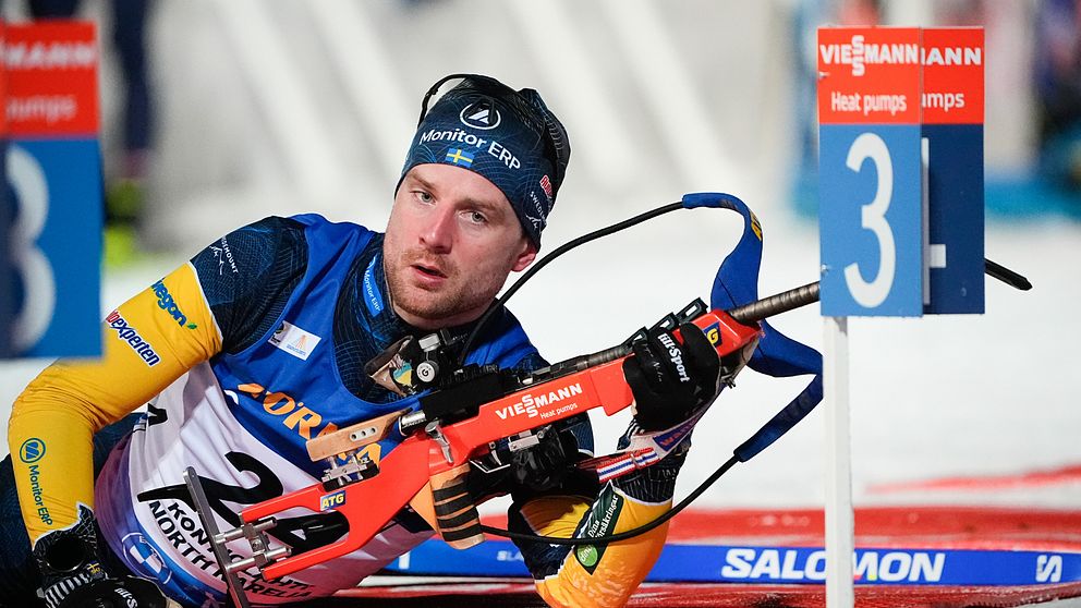 Skidskytten Jesper Nelin liggandes på skjutvallen under tävling iförd blågul dräkt, med bössan i handen,