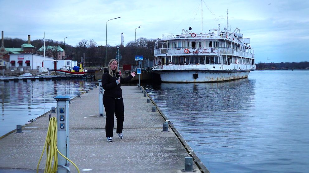 Reporter Cajsa Bengtsson går på brygga i Karlskrona, med Studentbåten förtöjd i bakgrunden. Mulet väder.