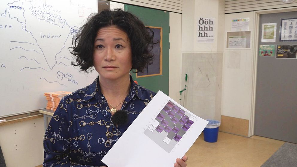 På Bilden syns Helen Nilsson, fackordförande för lärarfacket i Halmstad. Hon håller upp ett schema framför sig. Hon står i ett klassrum och i bakgrunden syns en whiteboardtavla.