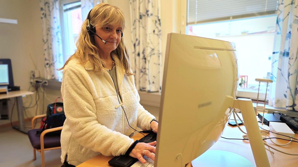 En kvinna med gråblont hår och ett headset på huvudet står framför en datorskärm