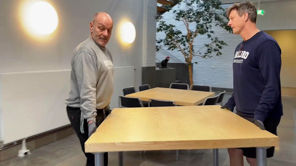 Två män bär ett trädbord i Teknikhuset, Örebro universitet.