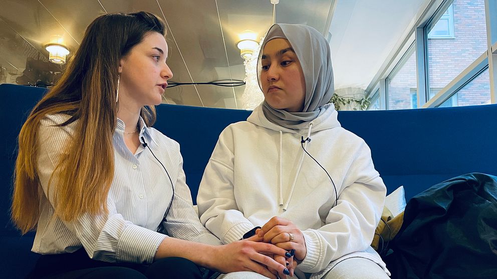 Två elever på Risbergska håller varandras händer och sitter på en blå soffa.