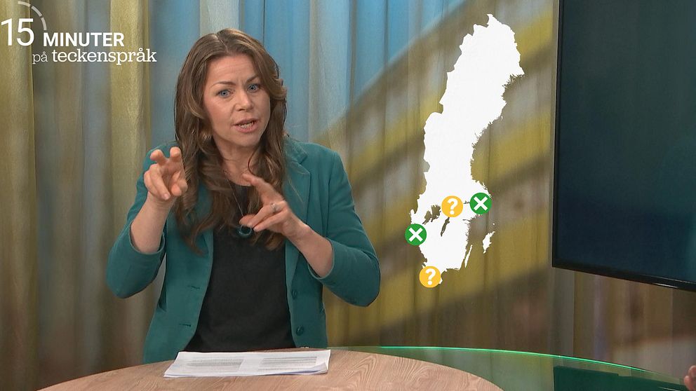 Maria Midbøe står i en studio och tecknar ”rekrytera”. Bredvid henne finns en karta över var det finns dövpsykiatriska mottagningar i Sverige. Stockholm och Västra Götaland har två gröna kryss som visar att det finns. Örebro och Skåne har gula frågetecken, som visar att framtiden är osäker.