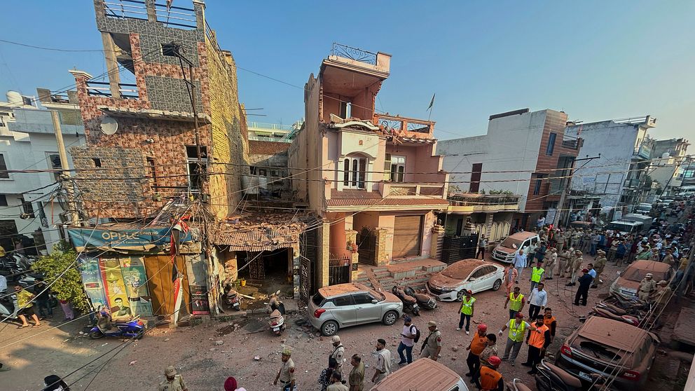 En förstörd byggnad i Jammu, Indien, efter en attack. Människor har samlats runt den skadade byggnaden och det syns damm på bilar.