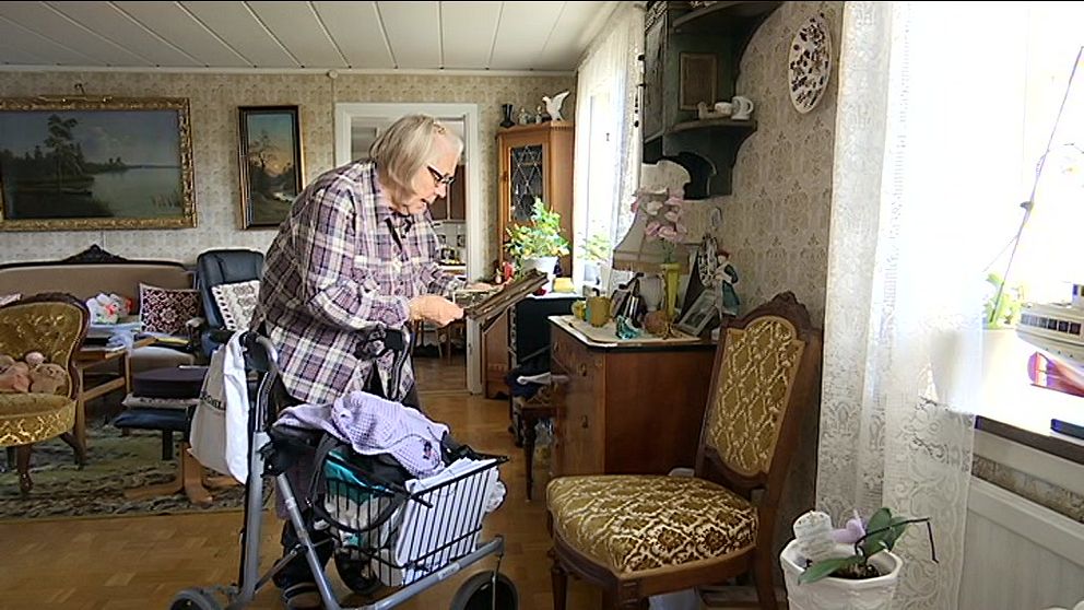 Äldre kvinna med rullator läser papper i ett hemtrevligt vardagsrum.