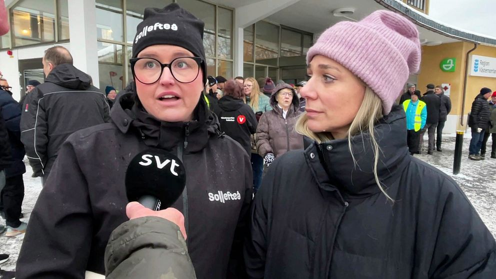 Två personer står i en grupp utanför en byggnad, där en av dem håller en mikrofon med SVT-logotypen. I bakgrunden syns en samling människor och en del vinterklädda personer.