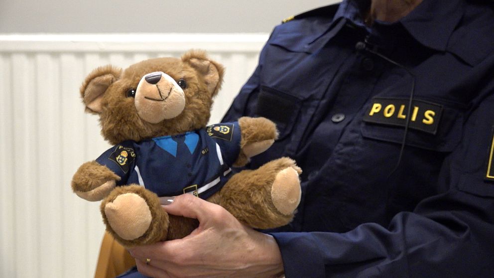Polis håller i en liten nallebjörn. Båda har likadana polisuniformer.